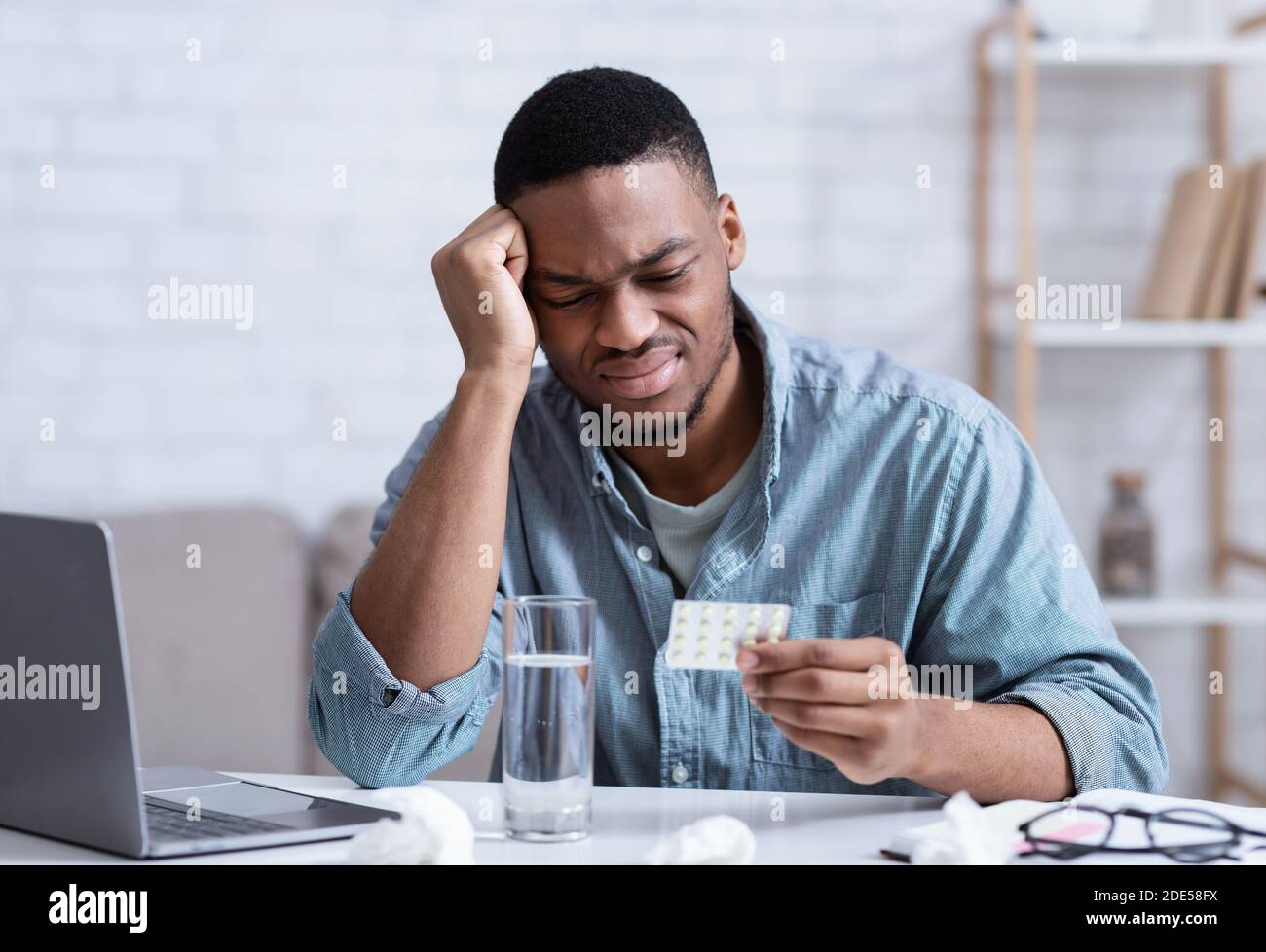 L'uomo africano che soffre di mal di testa leggere pillole Istruzione al posto di lavoro Foto Stock