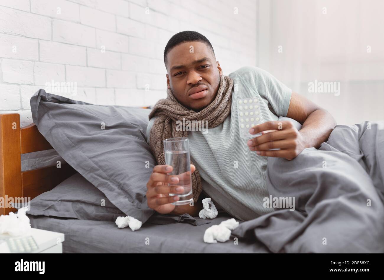 Uomo africano malato che mostra pillole di medicina giacente in letto interno Foto Stock