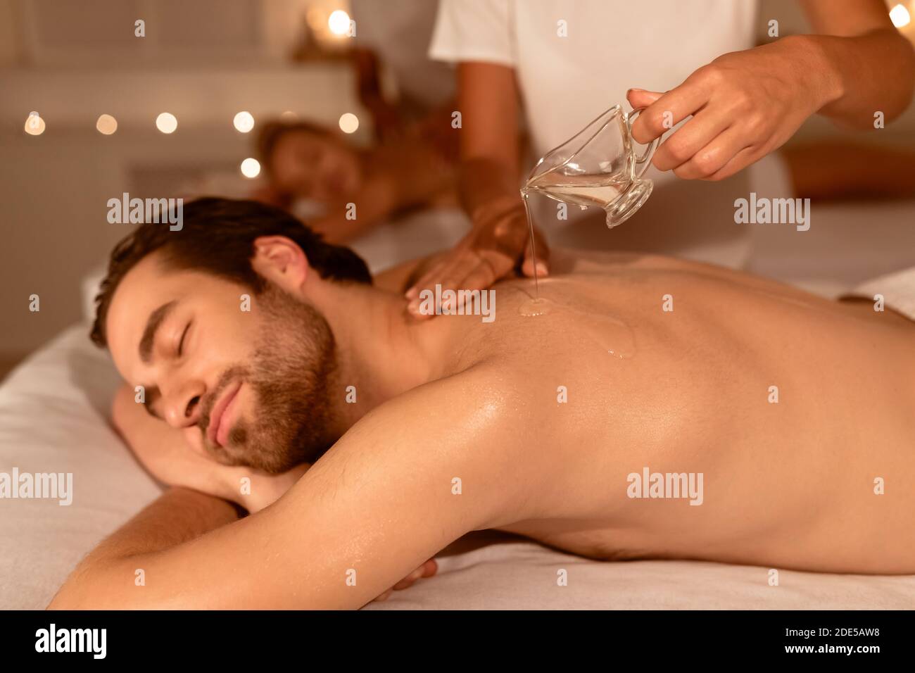 Massaggiatore che versa l'olio durante la terapia di massaggio delle Coppie alla Spa Foto Stock