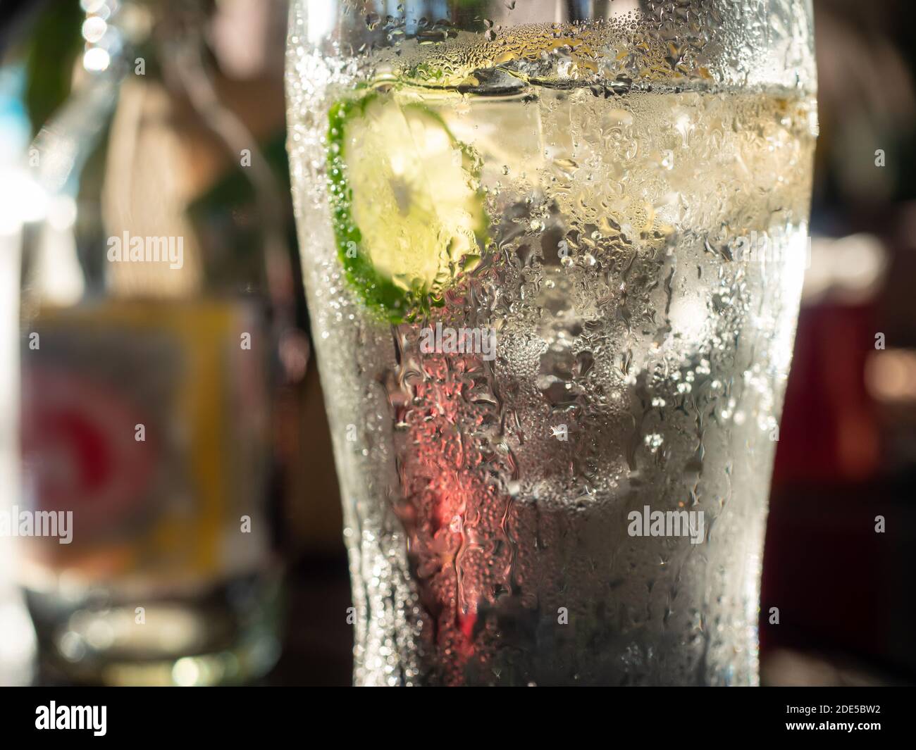 Bicchiere freddo di acqua soda con cubetti di ghiaccio e una fetta di calce. Acqua condensata all'esterno del bicchiere. Profondità di campo molto bassa con solo la co Foto Stock