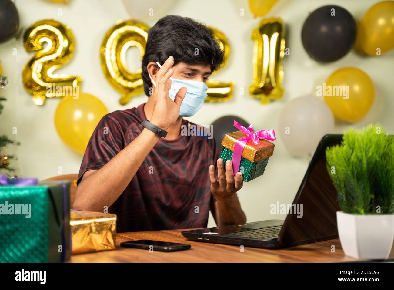 Focus selettivo sulla confezione regalo, giovane uomo con maschera medica ha ricevuto confezione regalo su videochiamata su laptop con 2021 nuovo anno di background - concetto di lontano Foto Stock