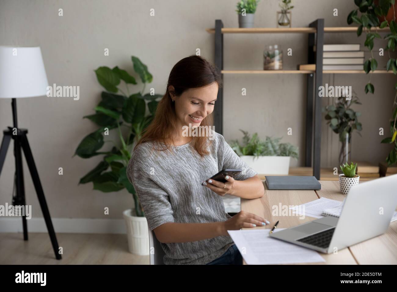 Distratto dal lavoro online del computer giovane donna che usa lo smartphone. Foto Stock