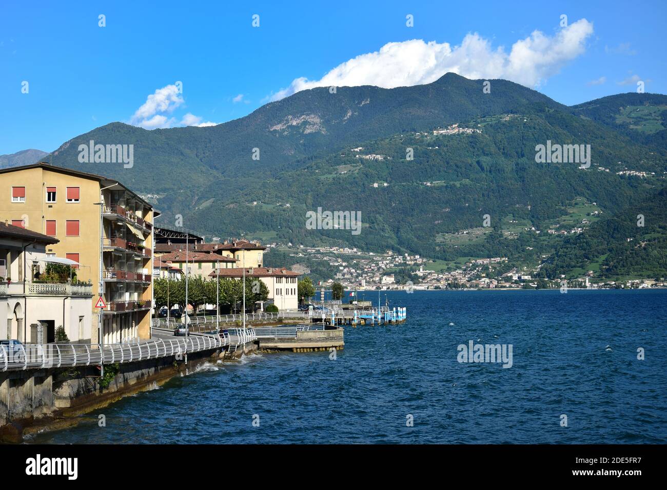 Un piccolo paese italiano con case e una strada lungo il lago. Montagne sull'altro lato del lago. Castro, Lago d'Iseo, Bergamo, Lombardia, Italia. Foto Stock