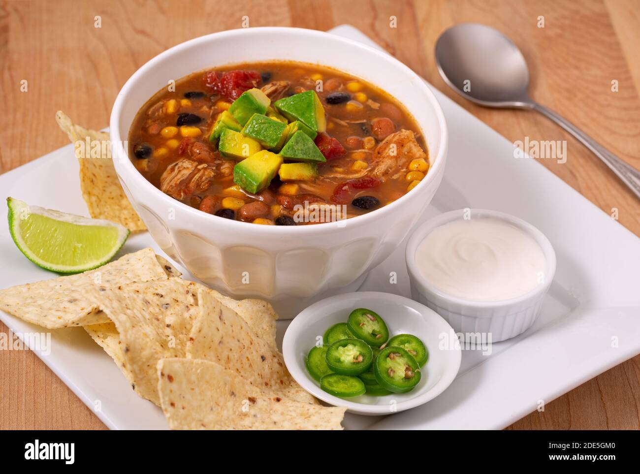Deliziosa ciotola di zuppa di pollo taco guarnita con avocado con contorni di peperoni, panna acida e patatine di tortilla Foto Stock