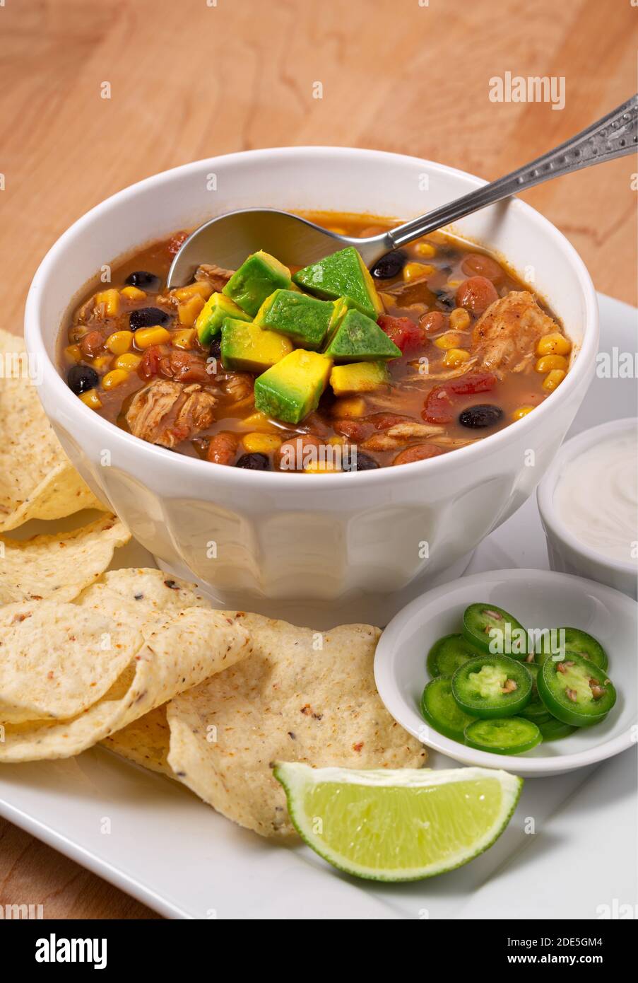 Deliziosa ciotola di zuppa di pollo taco guarnita con avocado con contorni di peperoni, panna acida e tortilla chips con spazio per la copia Foto Stock