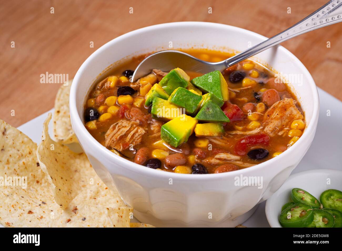 Deliziosa ciotola di zuppa di pollo taco guarnita con avocado con contorni di peperoni, panna acida e patatine di tortilla Foto Stock