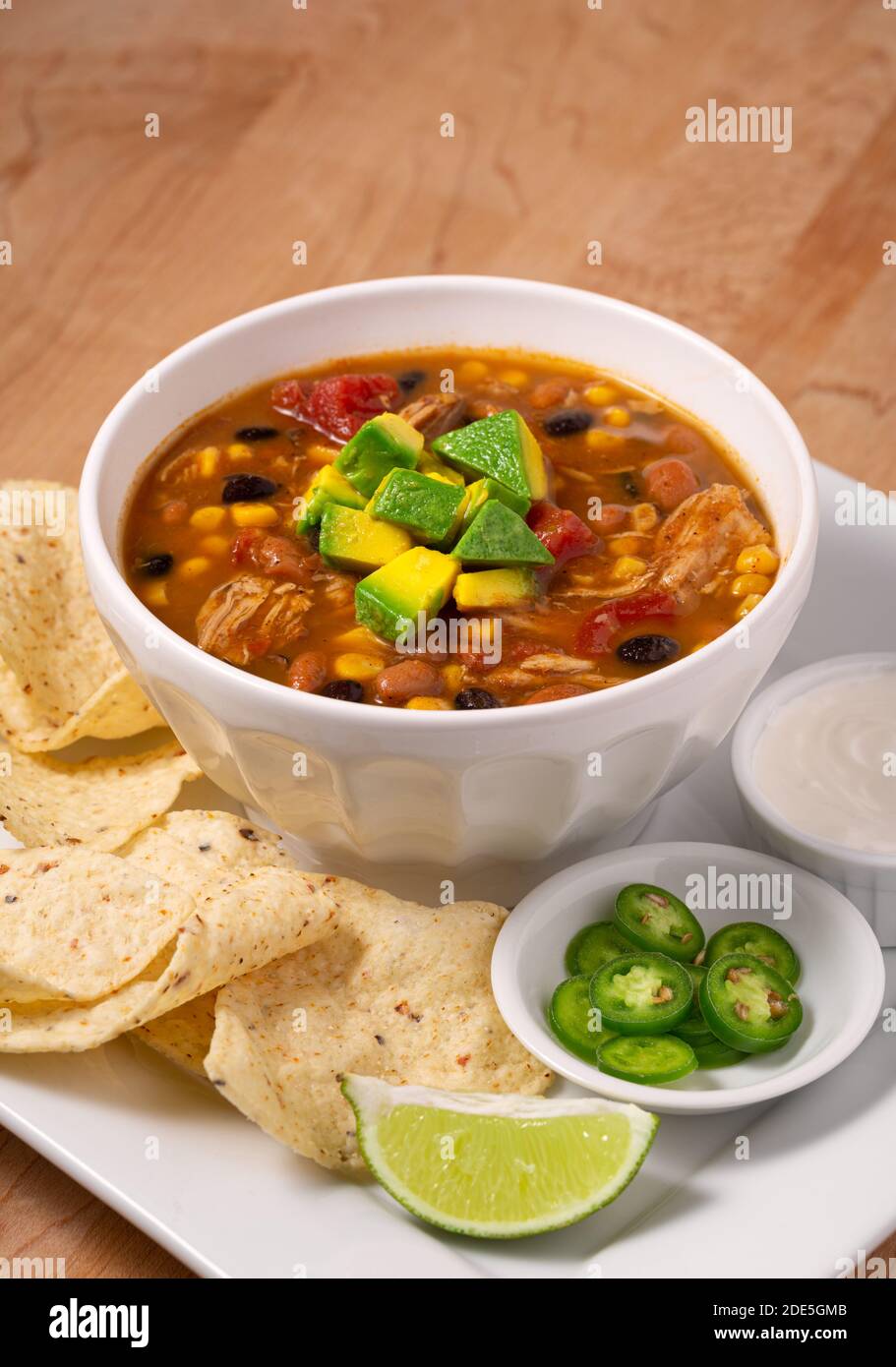 Deliziosa ciotola di zuppa di pollo taco guarnita con avocado con contorni di peperoni, panna acida e patatine di tortilla Foto Stock