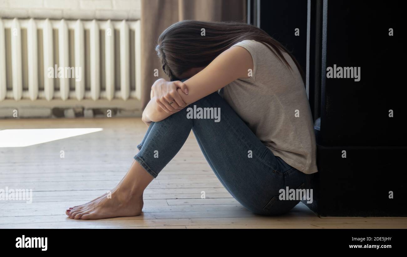 Una giovane donna infelice e frustrata che si inginocchiava, seduta sul pavimento Foto Stock