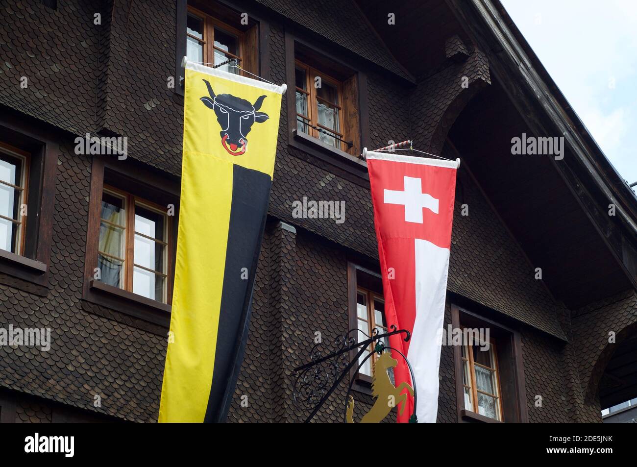 Striscioni del Cantone di Uri e della Svizzera appesi di fronte ad un tipico chalet in legno ad Andermatt, Svizzera Foto Stock