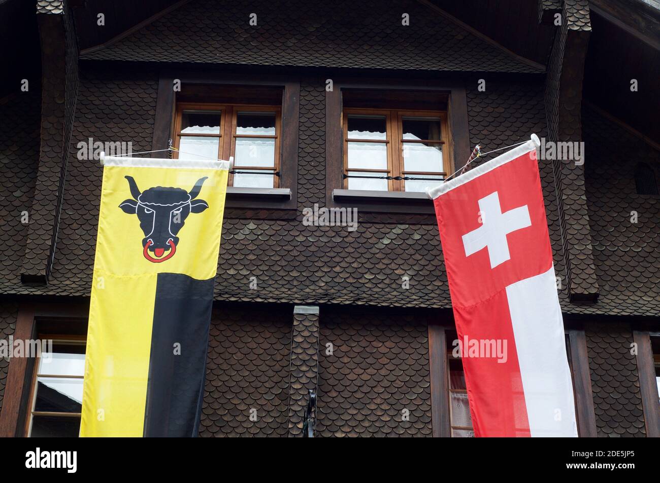 Striscioni del Cantone di Uri e della Svizzera appesi di fronte ad un tipico chalet in legno ad Andermatt, Svizzera Foto Stock