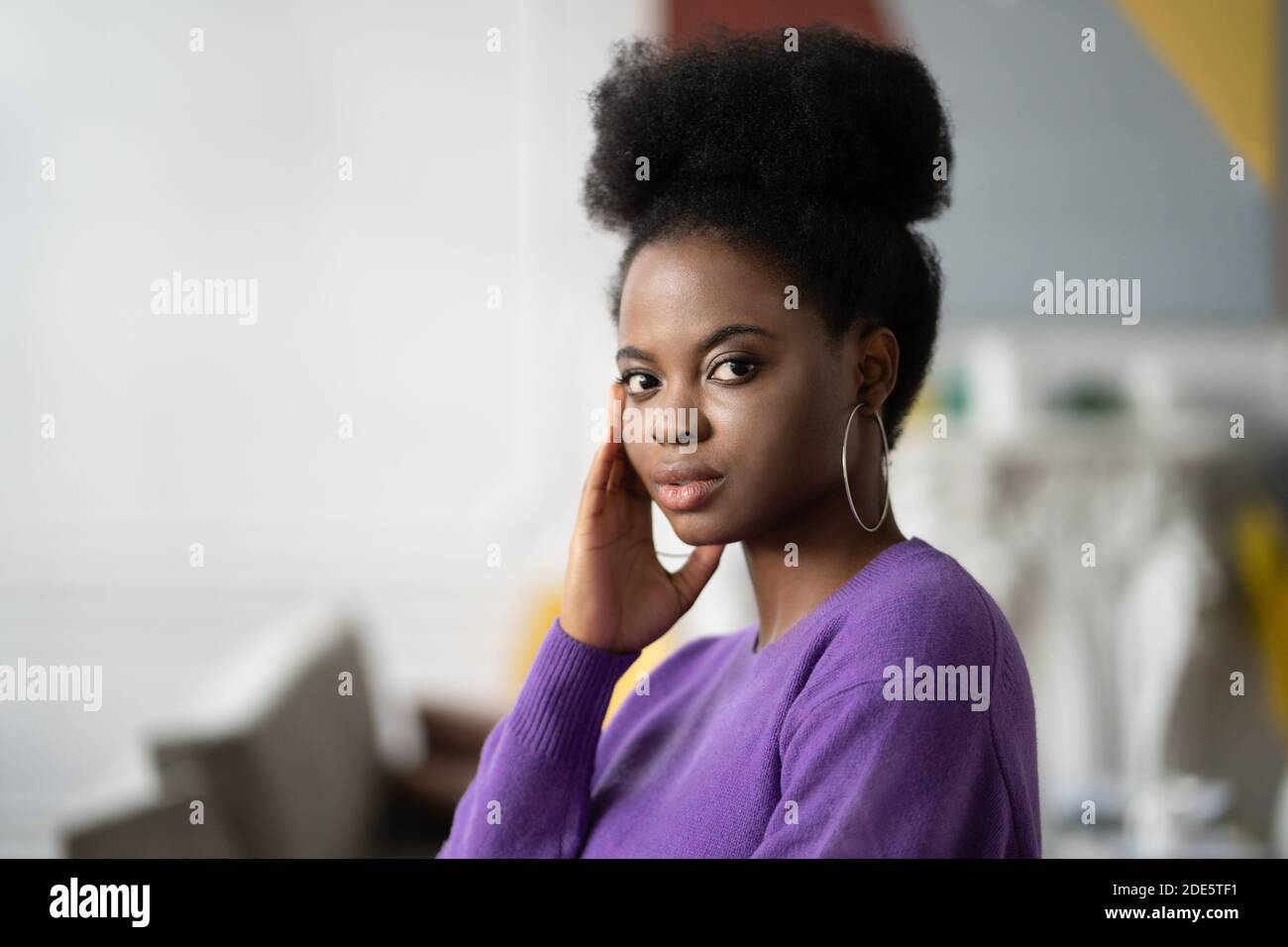 Ritratto di carina donna afro-americana con acconciatura riccia indossa maglione viola guardando la fotocamera. Foto Stock