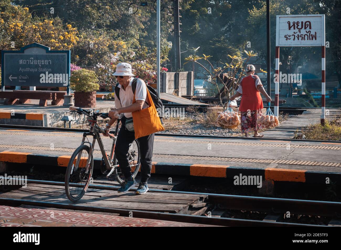 Thailandia; Feb 2020: Vita quotidiana in Thailandia, uomo tailandese che trasporta una bicicletta attraverso la ferrovia, vecchia donna tailandese che trasporta sacchetti di cibo per la vendita, attività mattutina Foto Stock