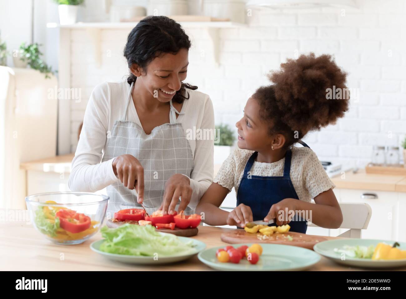Felice paziente mamma nera insegnare figlia piccola preparare una nutrizione sana Foto Stock