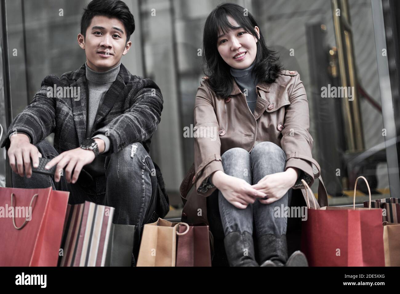 felice giovane coppia asiatica seduta a terra facendo una pausa mentre lo shopping in città Foto Stock