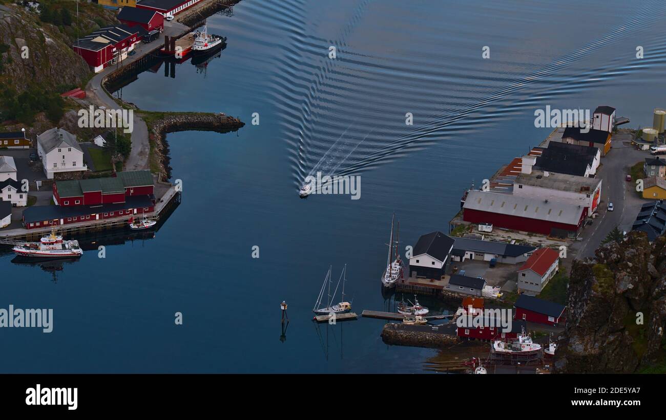 Ballstad, Vestvågøya, Lofoten, Norvegia - 08-29-2020: Veduta aerea della piccola barca con scia di onde che entrano nel porto del villaggio di pescatori Ballstad. Foto Stock