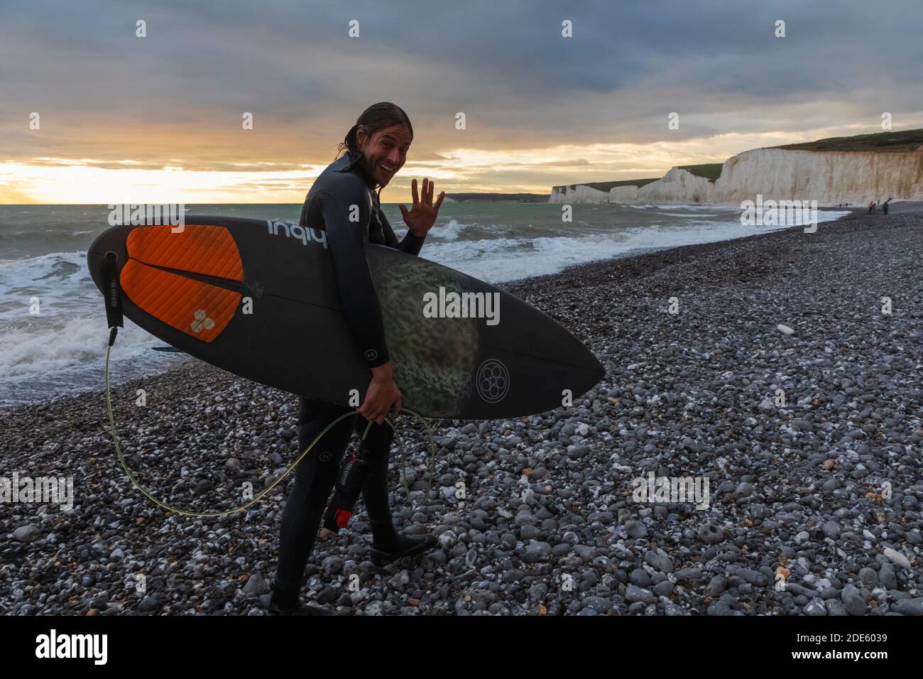 Inghilterra, East Sussex, Eastbourne, Birling Gap, The Seven Sisters Cliffs and Beach, Male Surfer Walking on Beach Caring Surfboard Foto Stock