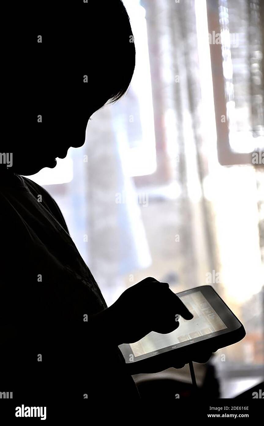 Silhouette di un bambino che usa un tablet, ipnotizzato e fissando lo schermo con una mascella caduta Foto Stock