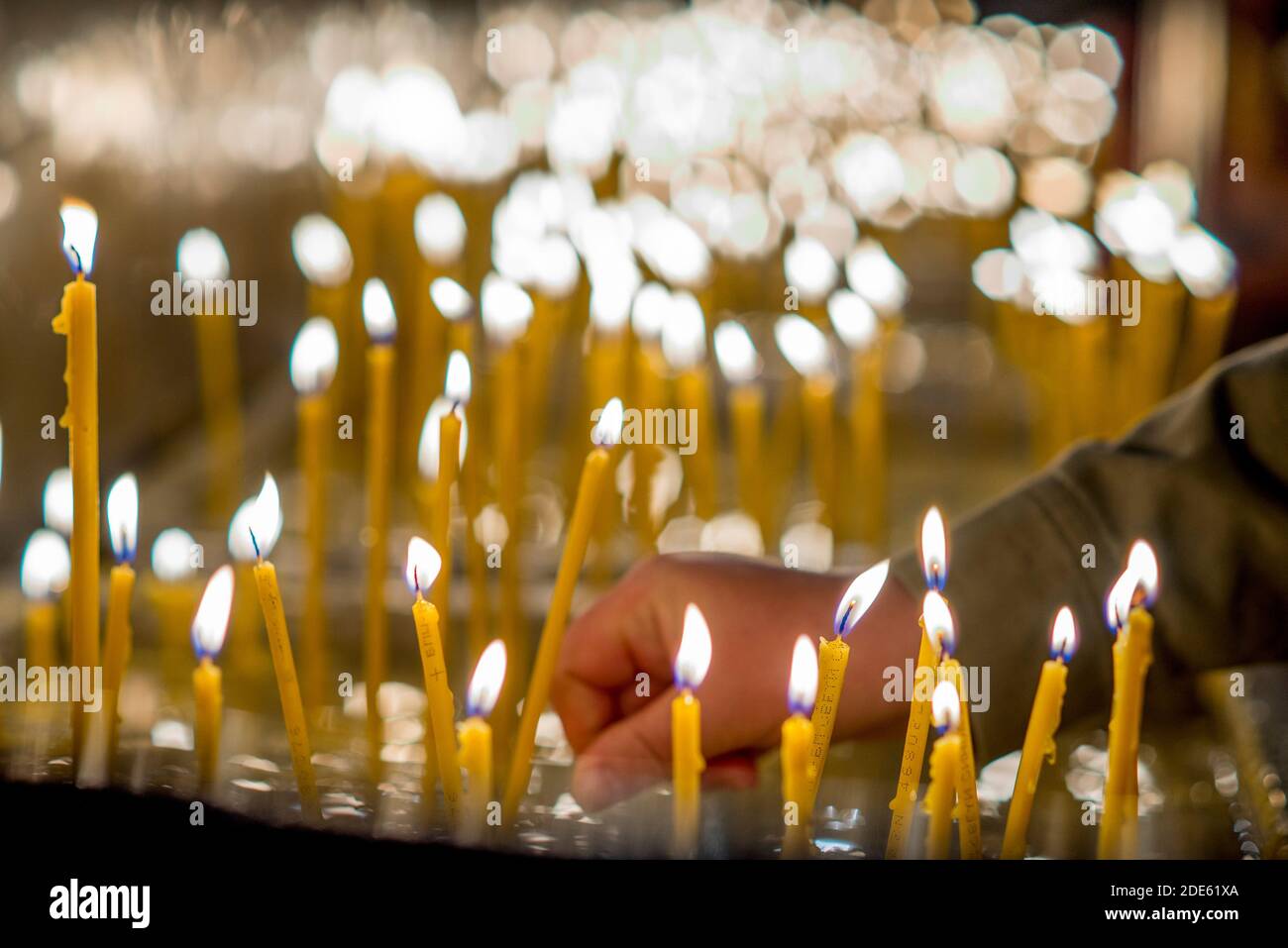Accendere una piccola candela tra molte altre candele in un chiesa ortodossa Foto Stock