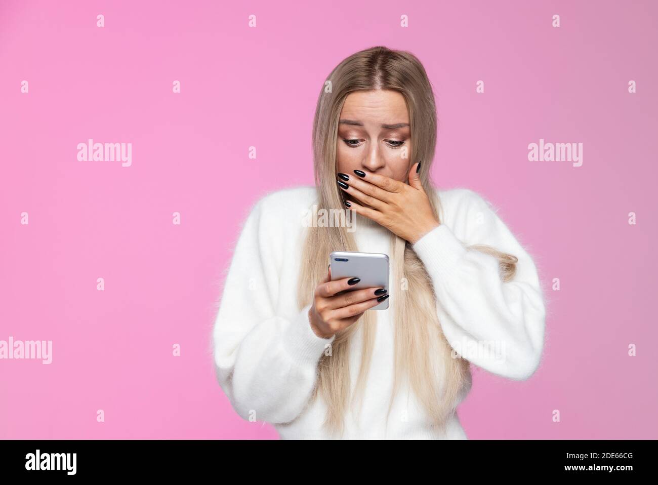 Donna ansiosa copre la bocca in shock, tenendo e guardando il cellulare smartphone, sorpresa reazione sul viso. Gesti di malvagità, espressione concep Foto Stock