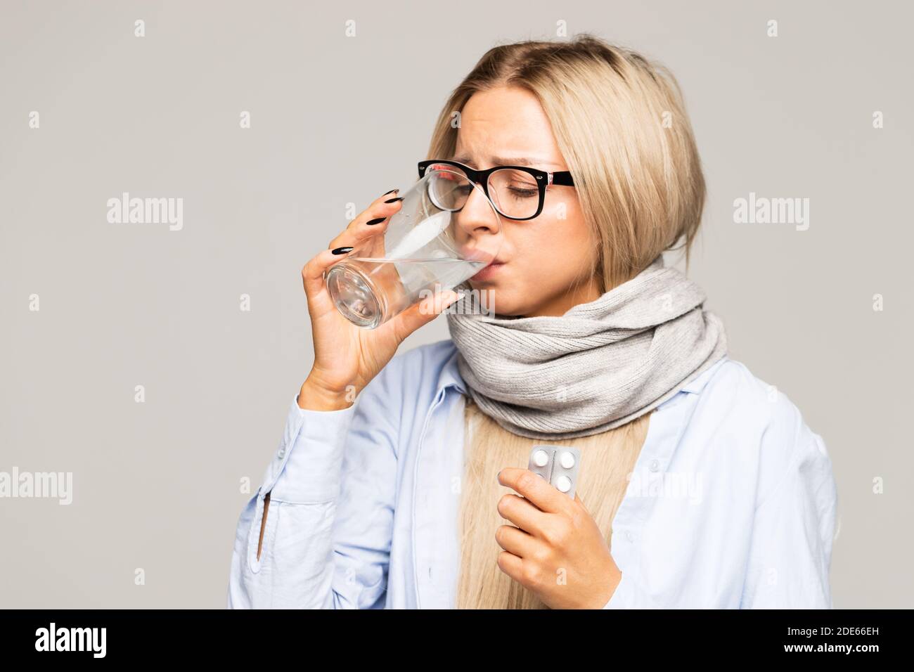 Donna con occhiali, camicia, sciarpa avvolti che tiene un bicchiere d'acqua e pillole. La donna malata ha influenza. Stagione fredda, malattia Foto Stock