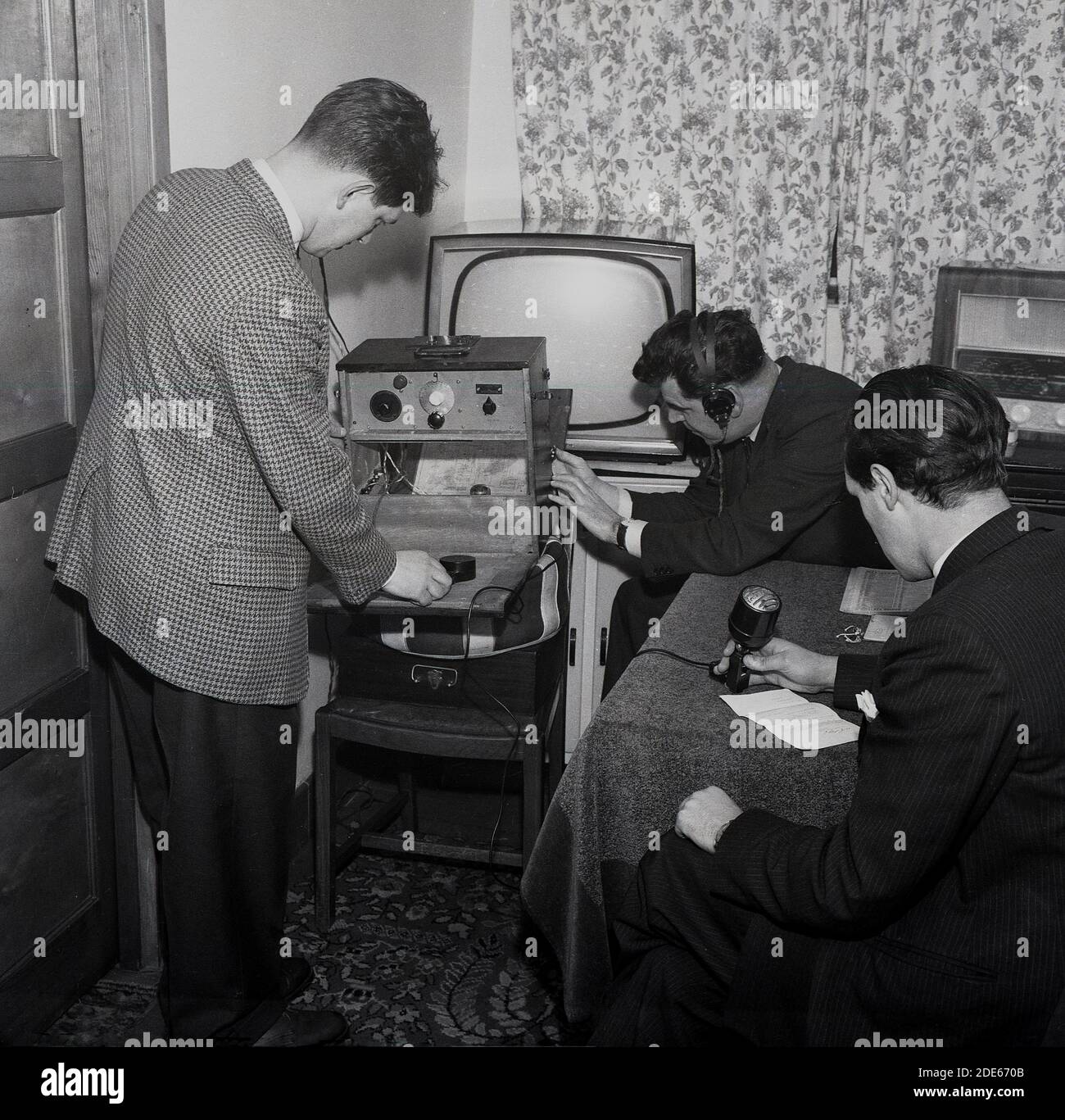 Anni '1960, storico, Pirate radio...inside una stanza in una casa, tre maschi coinvolti nella trasmissione radiofonica amatoriale....uno al microfono, uno con le cuffie e un altro che regola il trasmettitore, Londra, Inghilterra, Regno Unito. Foto Stock