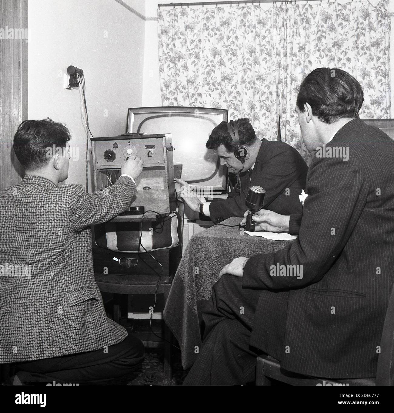 Anni '1960, storico, Pirate radio...inside una stanza in una casa, tre maschi coinvolti nella trasmissione radiofonica amatoriale....uno al microfono, uno con le cuffie e un altro che regola il trasmettitore, Londra, Inghilterra, Regno Unito. Foto Stock