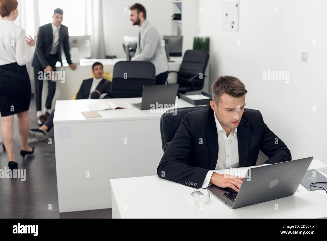 Un bel ragazzo giovane in un vestito di affari lavora in un ufficio di vendite di automobile. Negozio online in un computer portatile Foto Stock