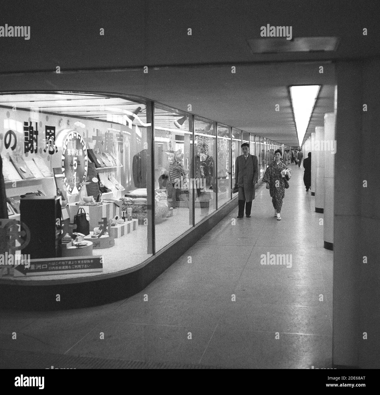 Anni '1960, storica, una coppia giapponese che cammina accanto alle vetrine di un negozio al dettaglio in un corridoio all'interno della metropolitana di Tokyo, Tokyo, Giappone. Foto Stock