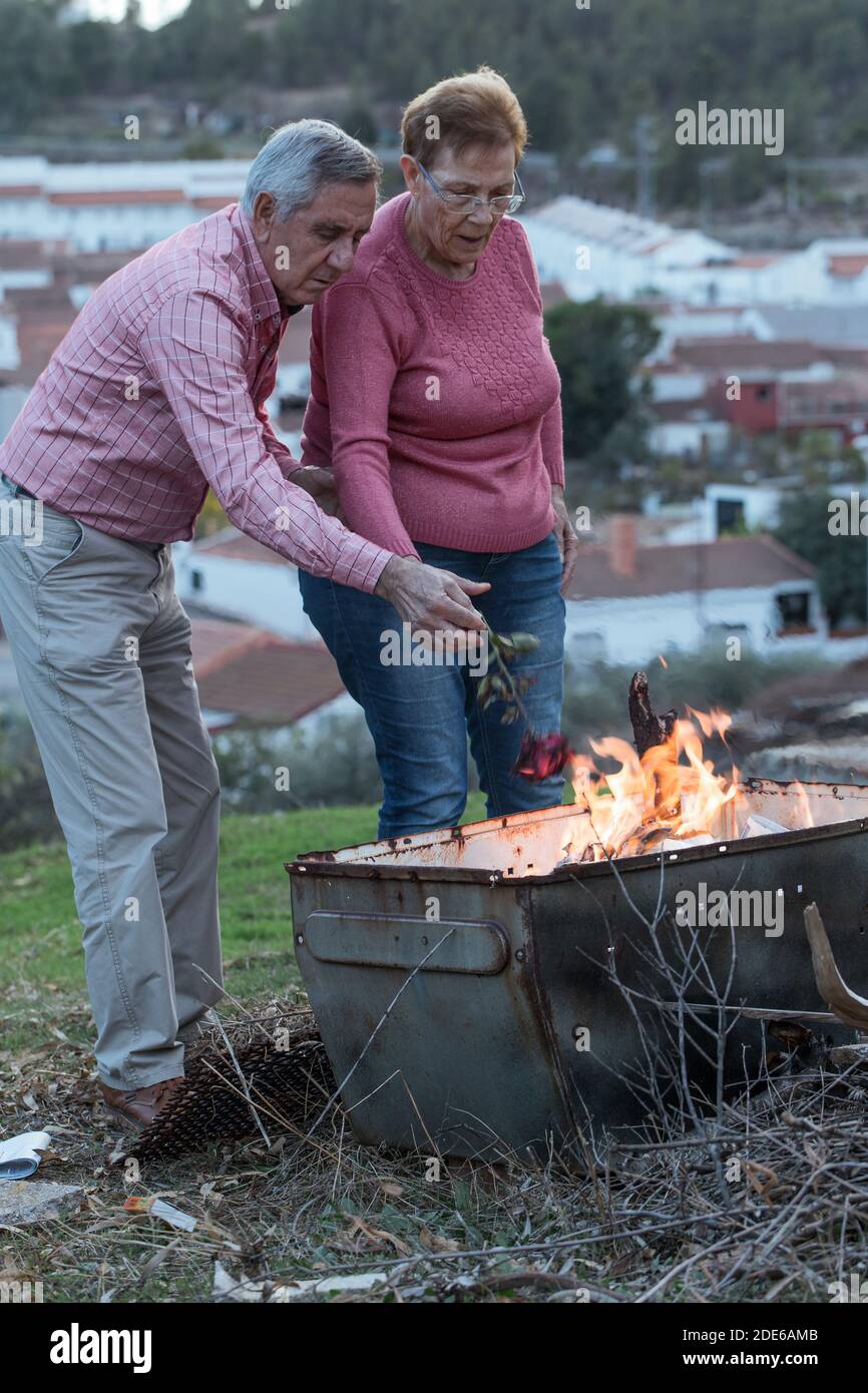 Coppia anziana in abiti casual mettendo rosa rossa in fiamme fuoco mentre rappresenta il concetto di problemi di relazione Foto Stock