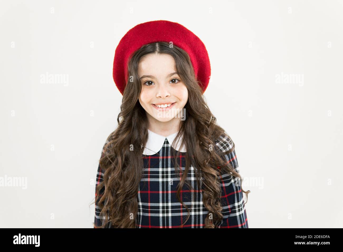 sentitevi straordinari. berretto francese parigino. come indossare un abito  a scacchi. capelli ricci lunghi ragazza. visita al parrucchiere. moda.  ragazza felice in uniforme. ritorno a scuola. look elegante per bambina  Foto stock -