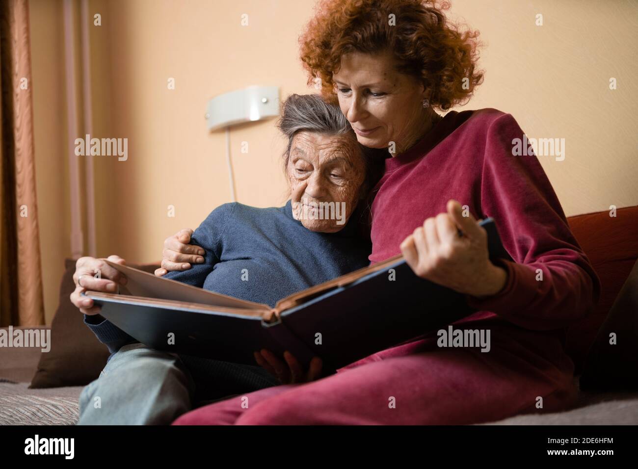 Positivo Signore invecchiato guardando album foto seduto divano a casa, amici allegri. Donna anziana e la sua infermiera matura guardando album fotografico. Nonna showi Foto Stock