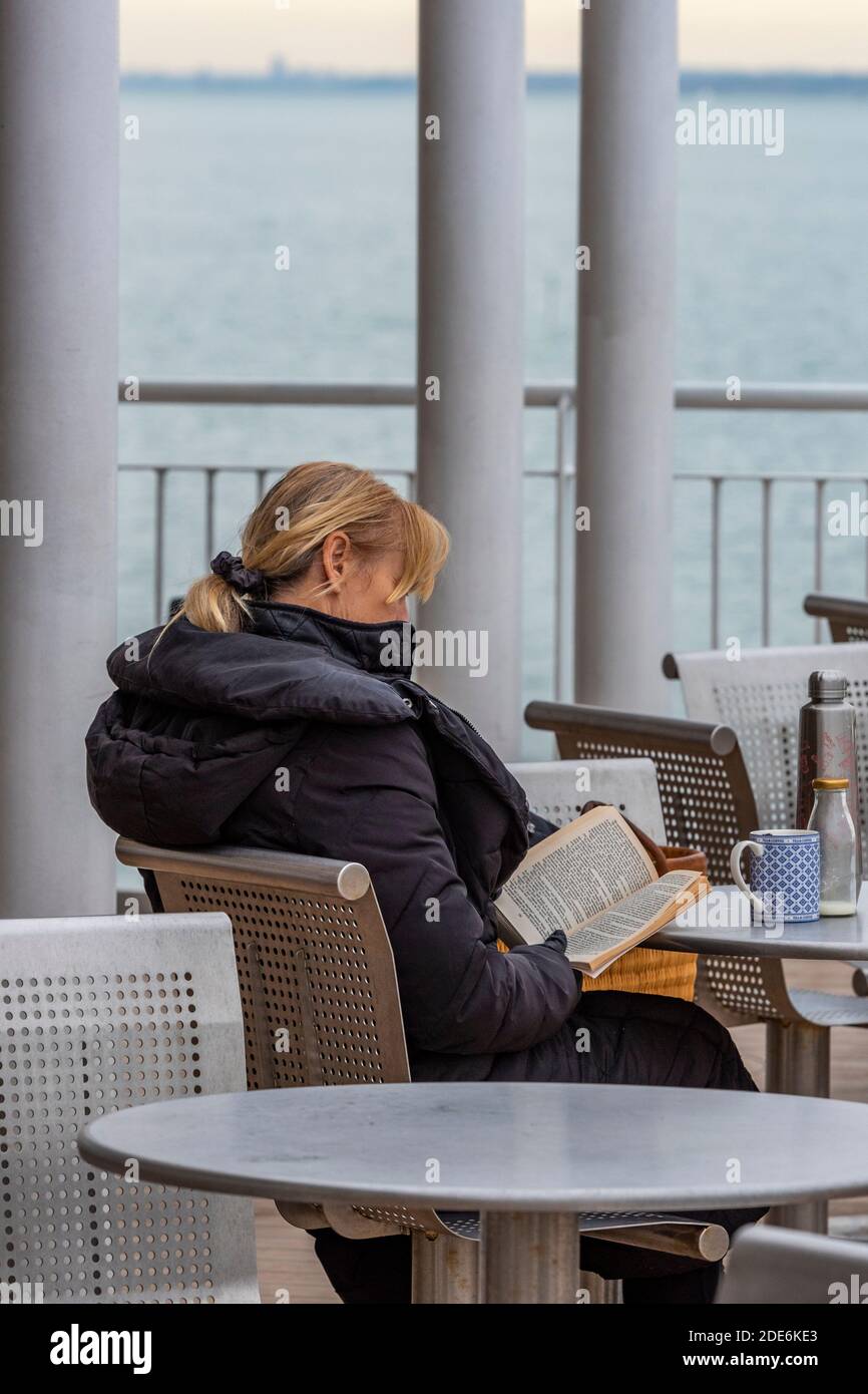 donna di mezza età seduta all'aperto leggendo un libro con una tazza di caffè. Foto Stock