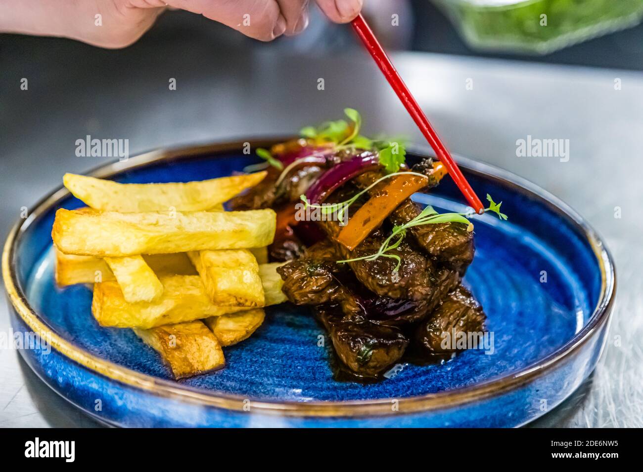 Un cuoco guarnisce un piatto di manzo brasato con cipolla rossa, peperoni ed erbe al ristorante Chakana di Birmingham, Inghilterra, servito con patate a cuneo croccanti – forse una variante del piatto nazionale peruviano Lomo Saltado. Foto Stock
