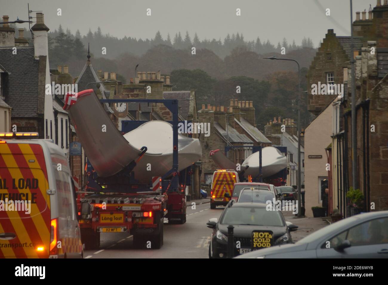 Un convoglio di autocarri che trasportano pale a turbina per un vento Fattoria sulla strada principale attraverso il villaggio di Golspie Nelle Highlands scozzesi Foto Stock