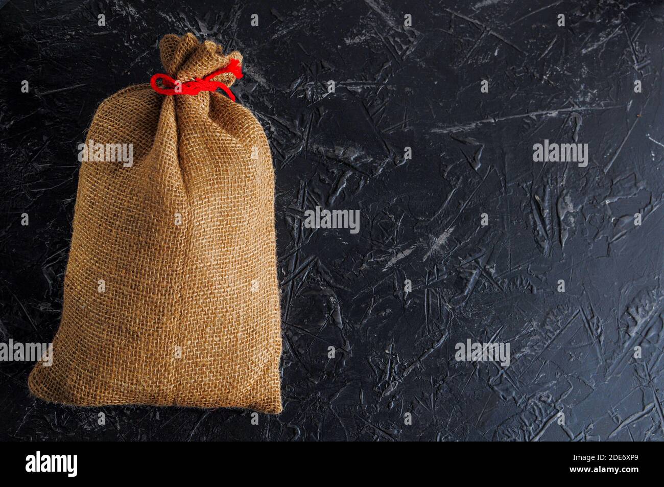 Una borsa di Natale riempita fatta di tela grossa, legata con spago rosso su uno sfondo scuro, spazio per il testo. Spazio di copia. Foto Stock