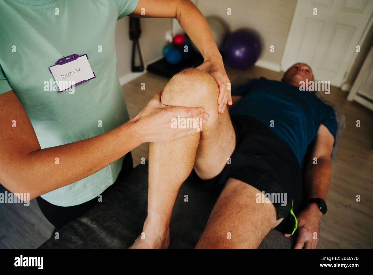 Massaggiatore femminile ginocchio curvante di maschio ferito sdraiato su letto di massaggio sportivo in sala di riabilitazione. Foto Stock