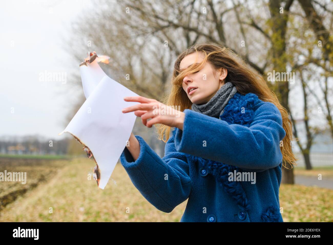 Bella giovane donna in camice blu rimanere al vento aperto area e tenere volare foglio di carta bruciante con fiamma e. smolder Foto Stock