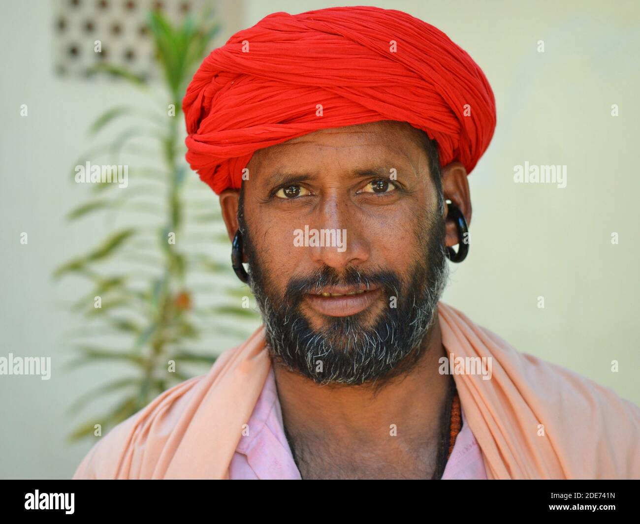 Il monaco di Gorakhnathi (Kanphata) yogi, di mezza età e turbanato rosso, con i grandi orecchini di firma dell'ordine religioso indù di Gorakh-Nath, rappresenta per la telecamera. Foto Stock