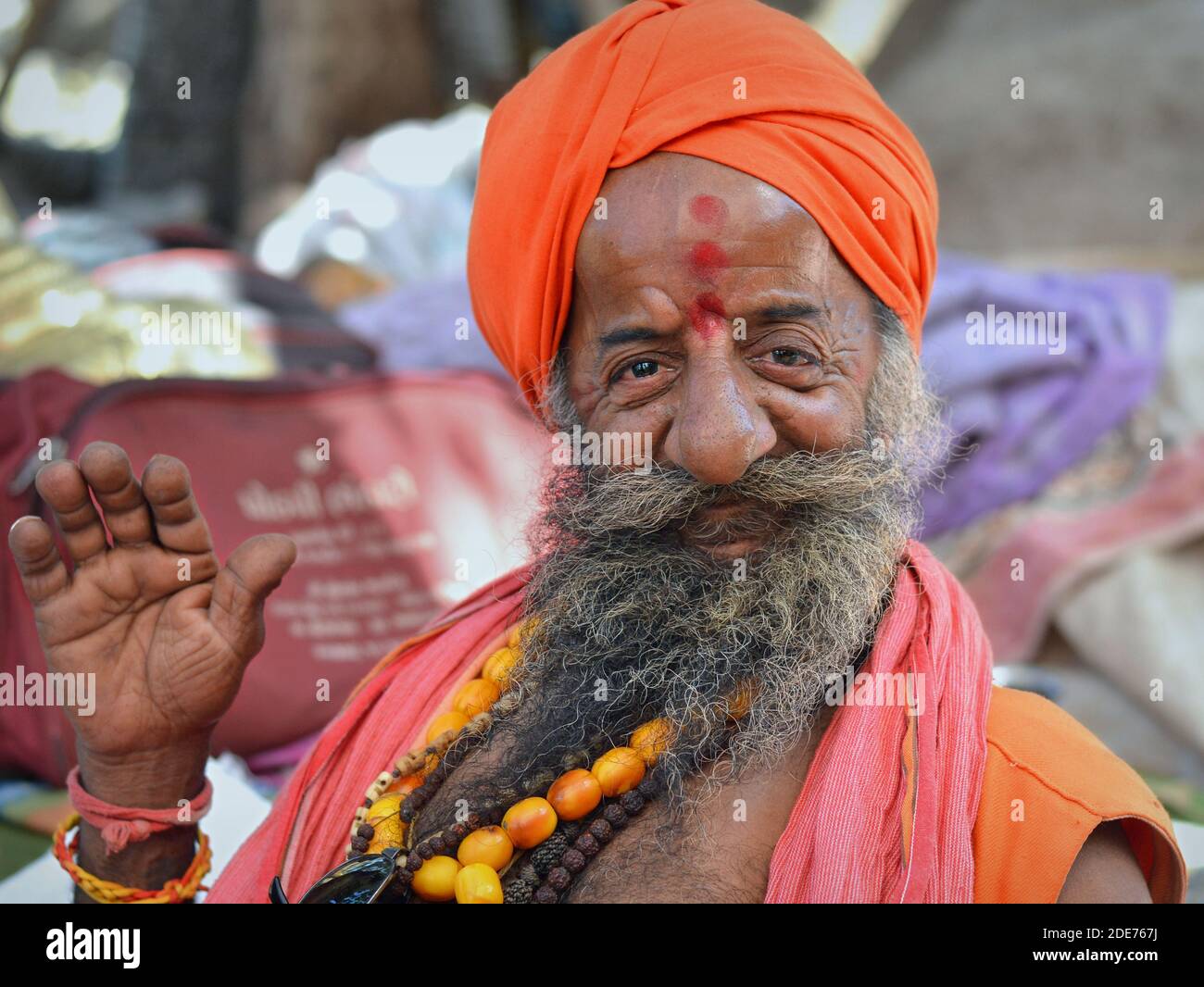 Felice vecchio indù indiano sadhu (baba, guru) alza la sua mano destra con la palma in avanti per dare una benedizione durante la fiera di Bhavnath (Shivratri Mela). Foto Stock