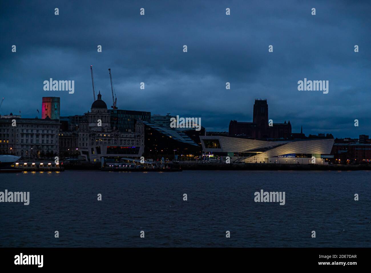 Il moderno Museo di Liverpool con la sua facciata bianca curva, e dietro di esso la torre illuminata della Cattedrale di Liverpool (Chiesa d'Inghilterra), definiscono lo skyline serale di Liverpool, in Inghilterra, visto attraverso il fiume Mersey dalla penisola di Wirral vicino Birkenhead. Foto Stock