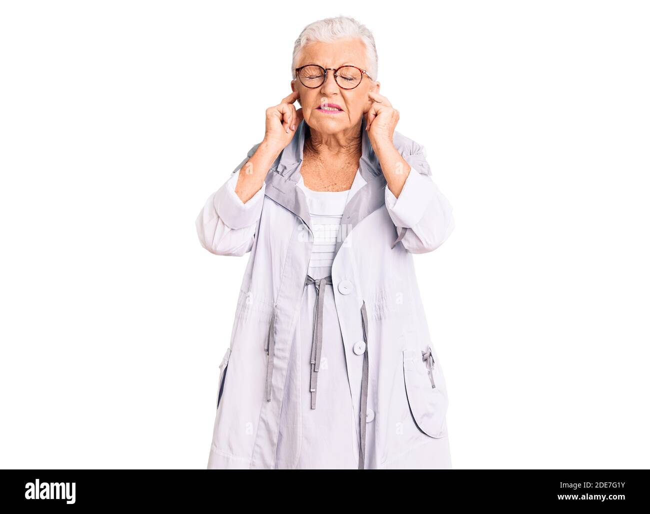 Donna anziana bella con gli occhi blu e capelli grigi indossare vestiti e occhiali casual che coprono le orecchie con le dita con fastidioso espressione per il nois Foto Stock