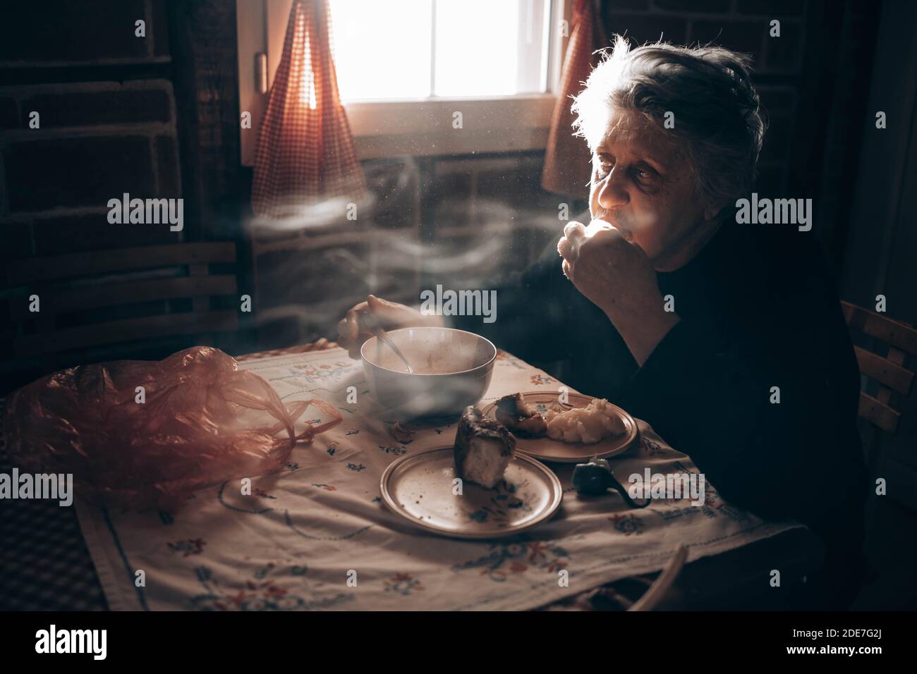 Donna anziana seduta da sola al tavolo, mangiando un pasto Foto Stock
