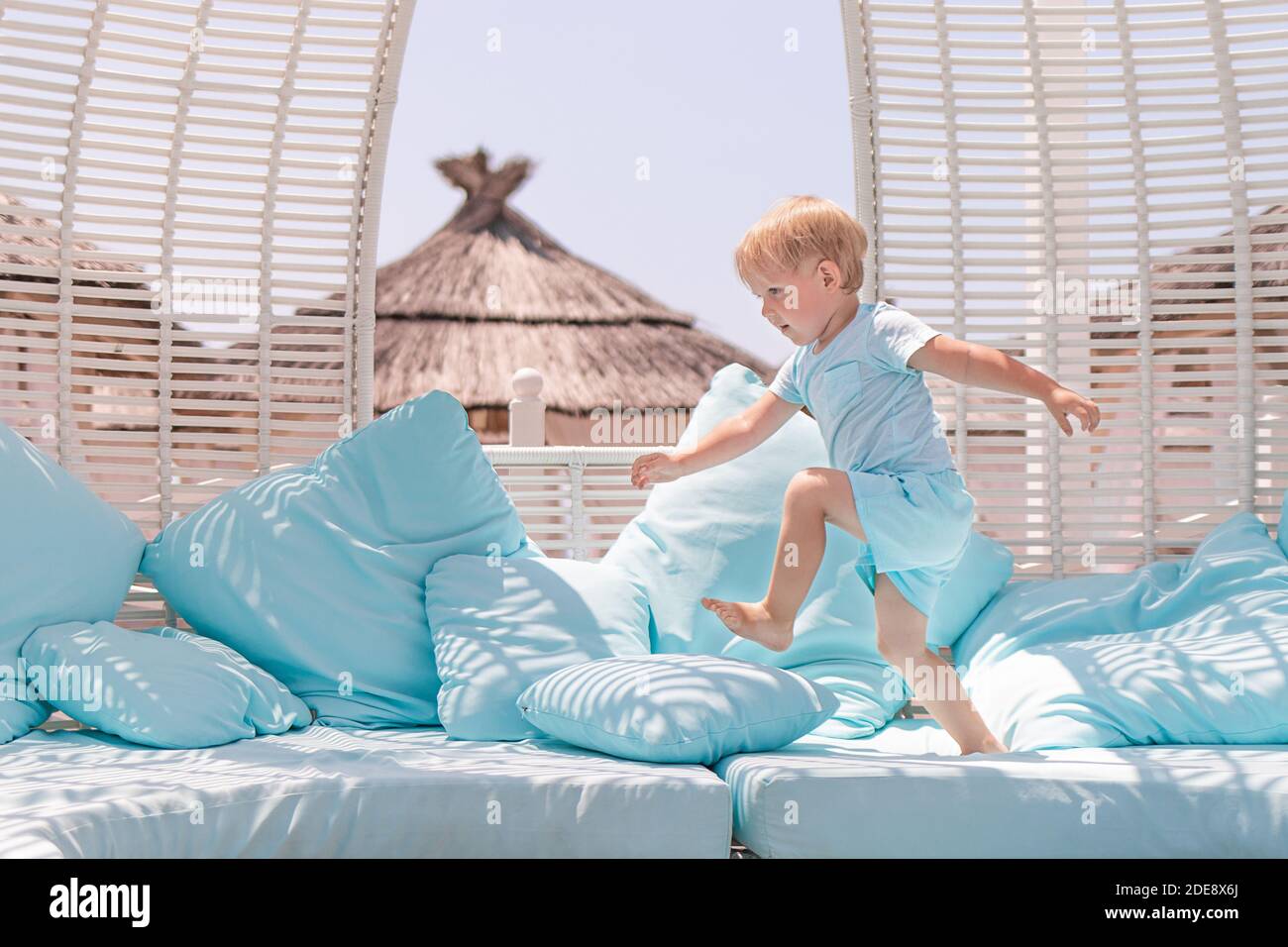 Bambino caucasico bambino bambino ragazzo toddler in caffè salta e corre su cuscini blu pastello. Concetto di problemi di vacanza e di vacanza con bambini attivi. Foto Stock