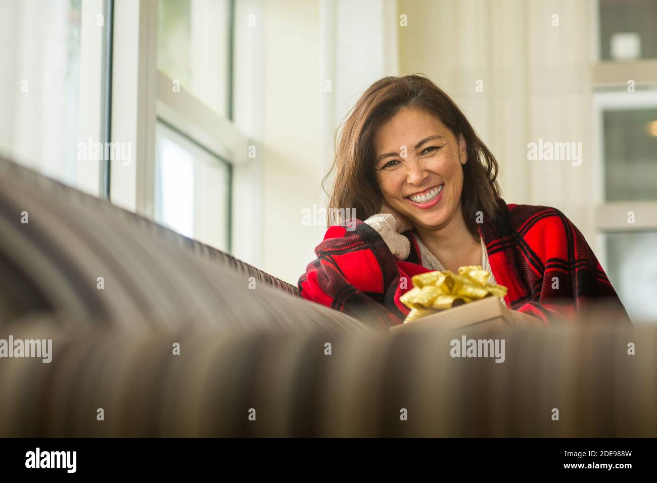 Donna asiatica che tiene un regalo seduto sul divano. Foto Stock