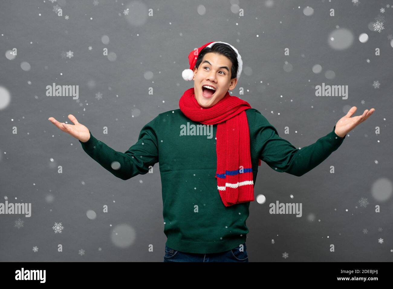 Eccitato giovane uomo asiatico indossare abito a tema natalizio con aperto gesto delle palme in nevicata Foto Stock