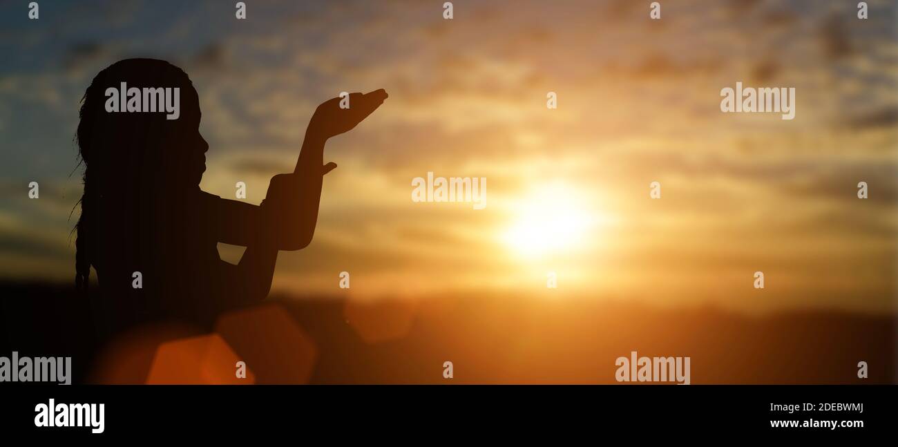 Silhouette di bambina cristiana aprire le mani a pregare per la benedizione da dio a sfondo tramonto. Foto Stock