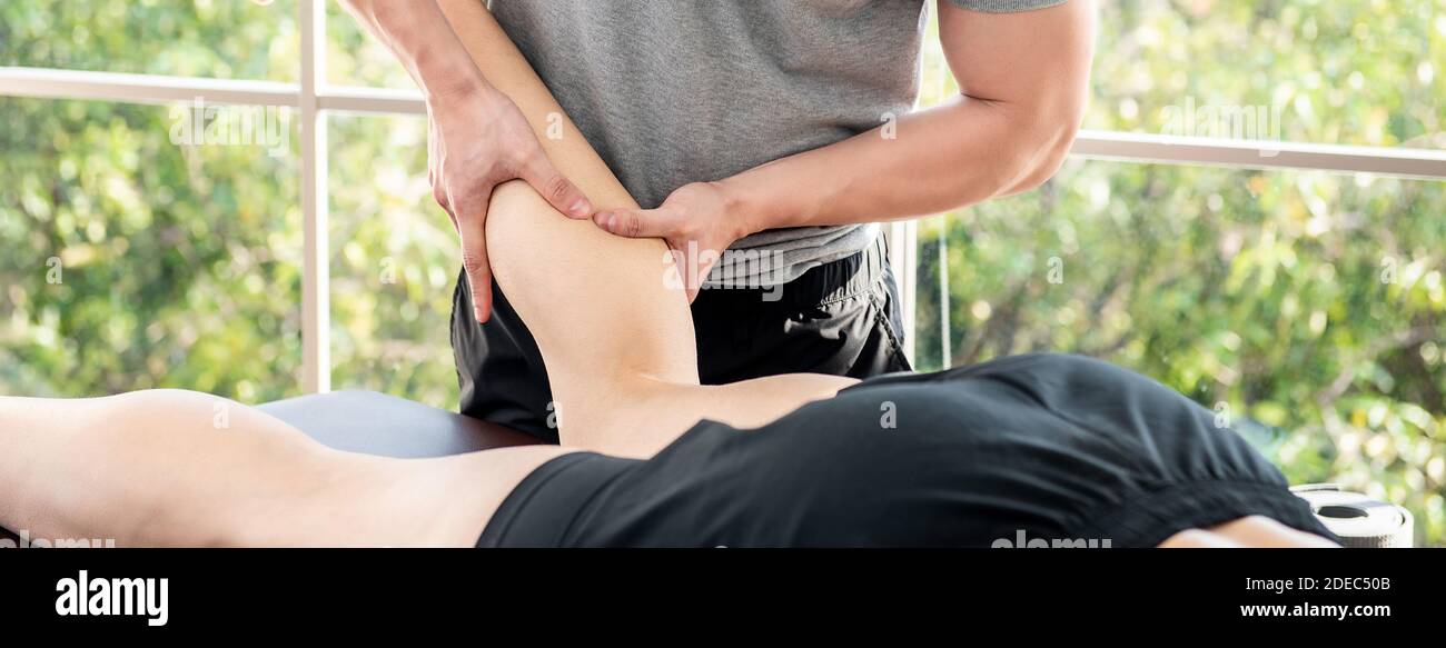Terapista maschile che dà massaggio gambe e polpaccio ad atleta paziente sul letto in clinica, sport fisica concetto di terapia Foto Stock