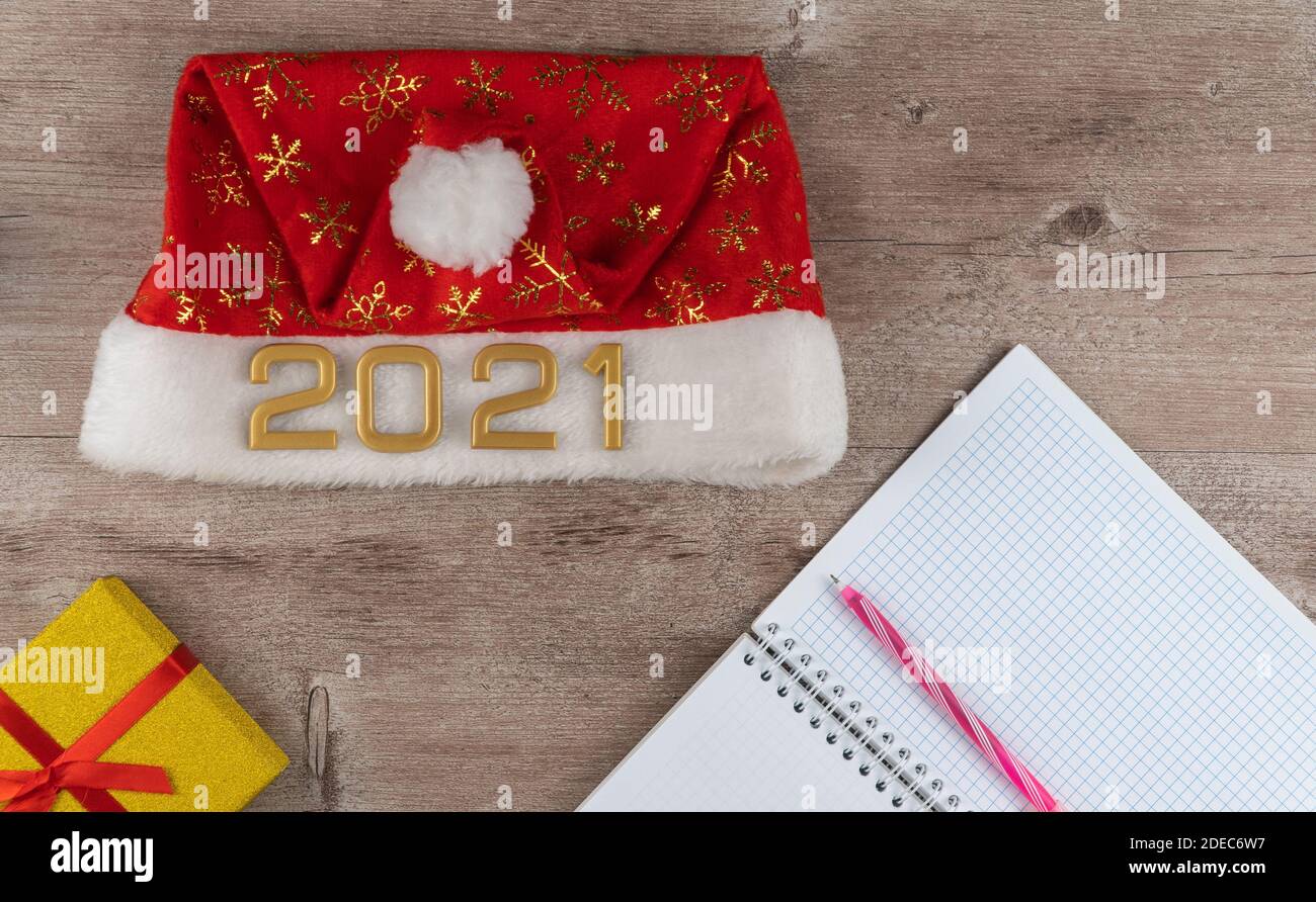 Cappello di Babbo Natale con numeri 2021 e pianificatore quotidiano. Il concetto di fare desideri a Natale. Wishlist su uno sfondo di legno Foto Stock