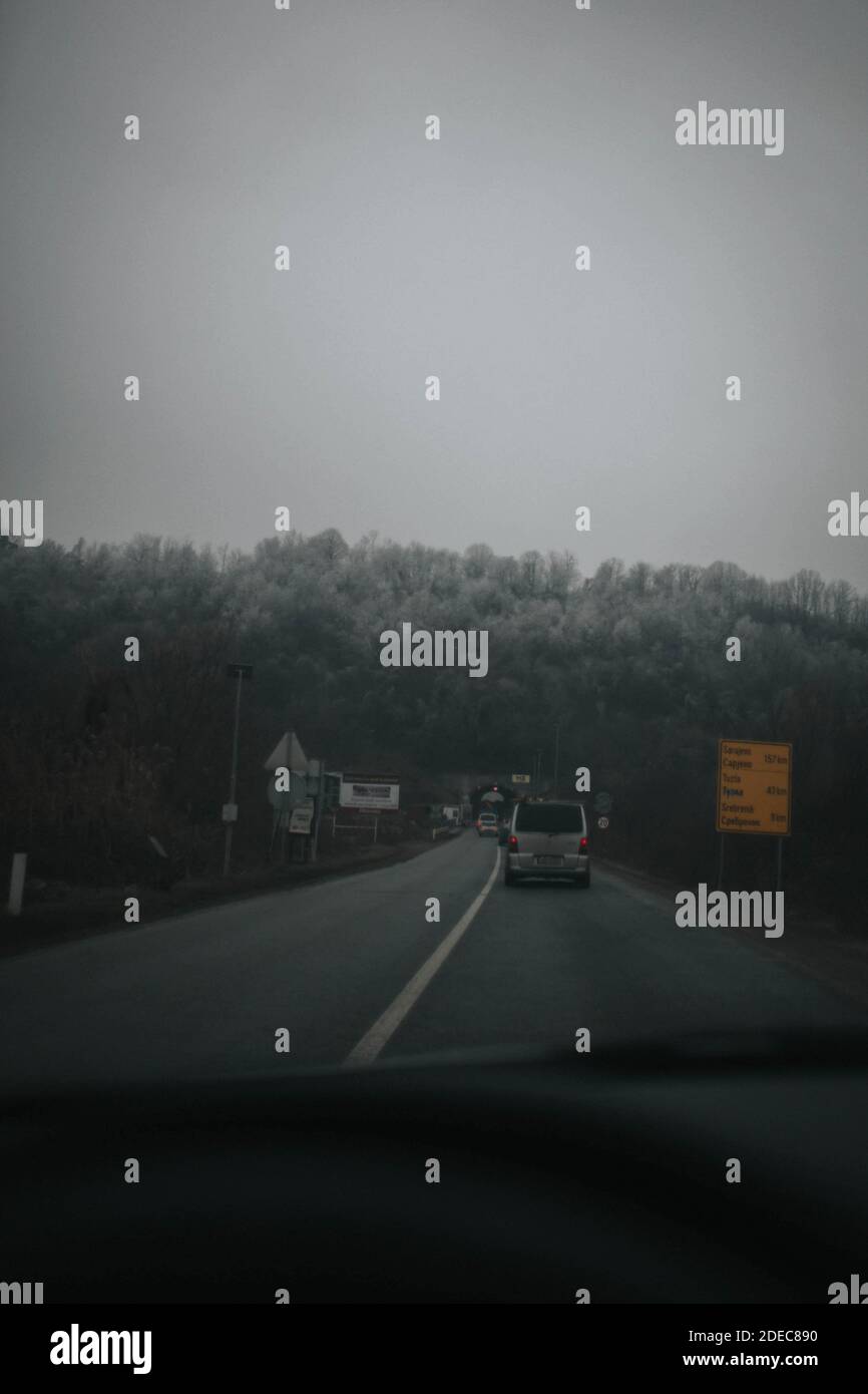 Un'immagine verticale in scala di grigi delle vetture che guidano sul strada circondata da alberi da una macchina Foto Stock