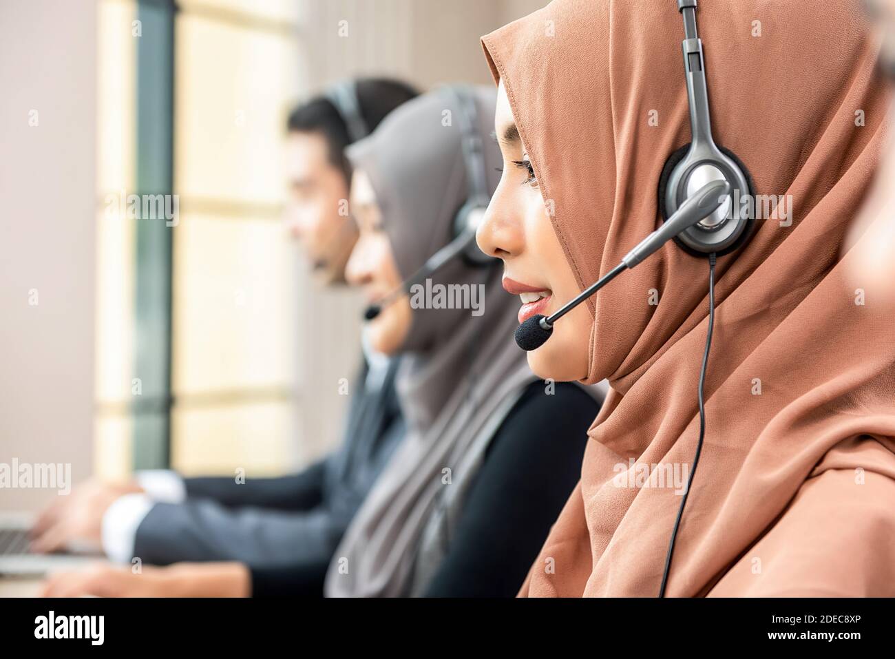 Donna musulmana che indossa cuffie con microfono e lavora come operatore di assistenza clienti con il team nell'ufficio del call center Foto Stock